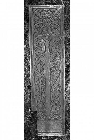 Black and white photo of a rectangular carved grave slab showing a large sword and foliate decoration surrounding it 